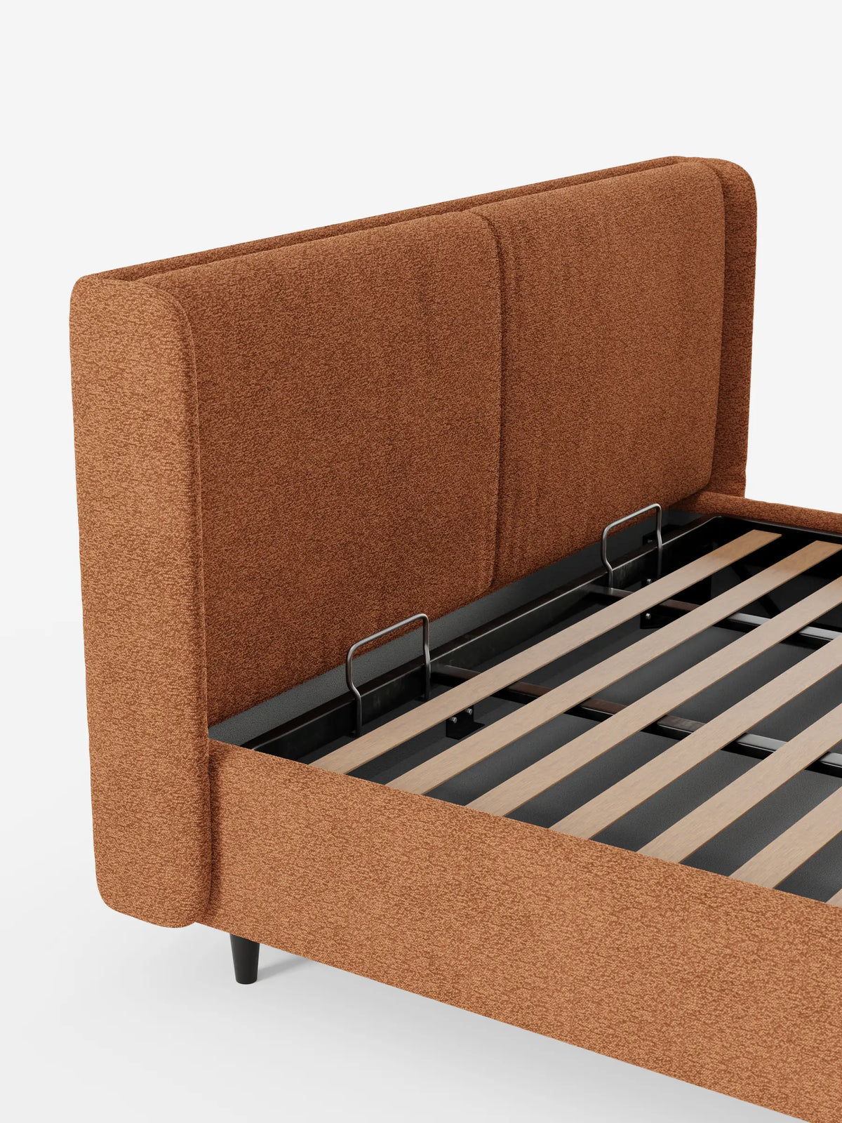 Il letto di design VALKIRIA con contenitore e testiera avvolgente - 2 cuscini imbottiti e tessuto Oeko-Tex® presenta una testiera dalla trama particolare, color arancio bruciato, e una piattaforma sollevabile che rivela doghe in legno chiaro e una struttura di sostegno in metallo.