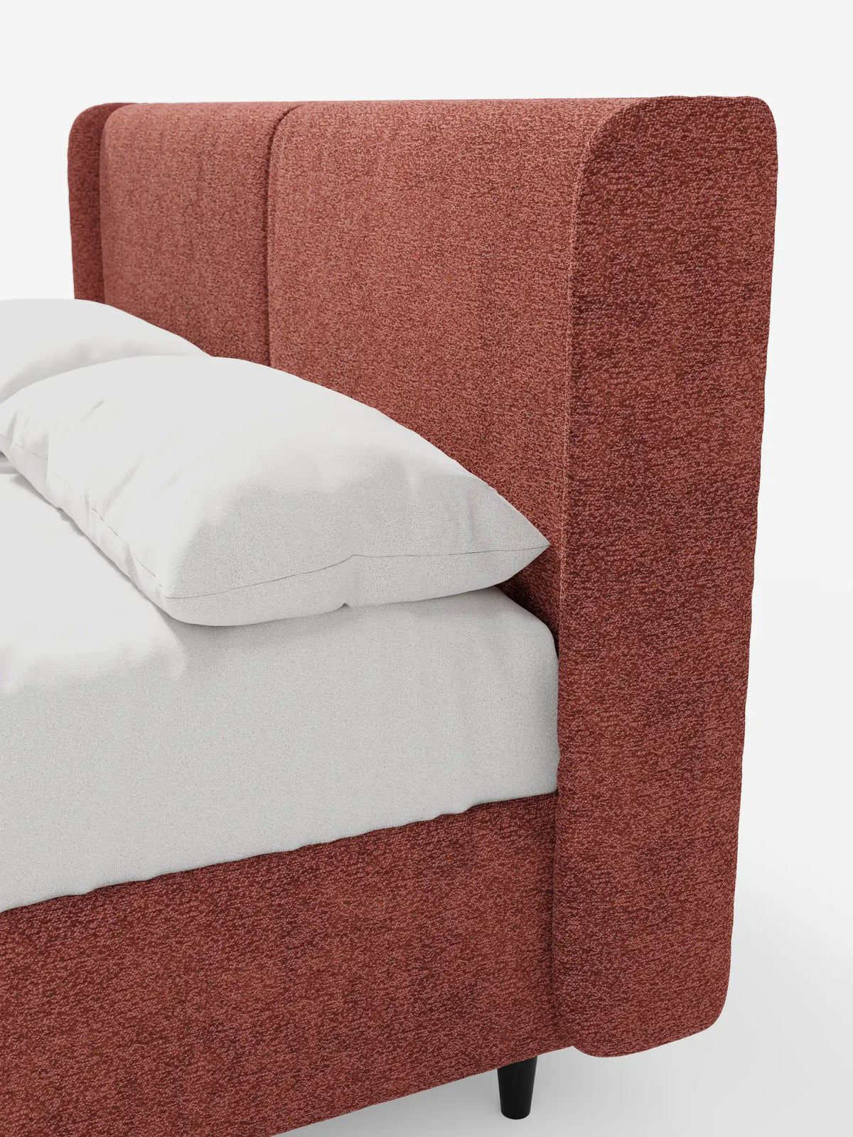 Un primo piano di un letto di design VALKIRIA con contenitore e testiera avvolgente, caratterizzato da una struttura in tessuto testurizzato color ruggine, una testiera avvolgente con cucitura verticale, due cuscini bianchi e piedini cilindrici scuri.