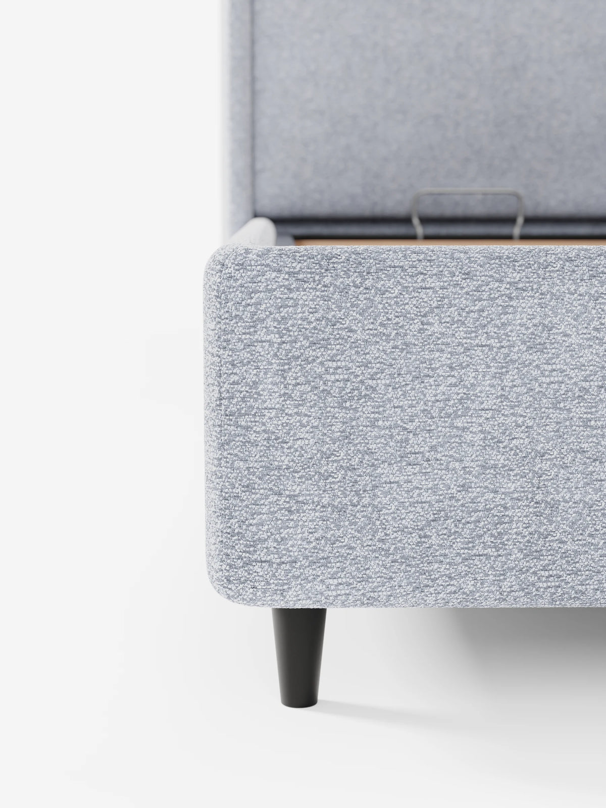 Il letto di design VALKIRIA con vano contenitore e testiera avvolgente – 2 cuscini imbottiti e tessuto Oeko-Tex® – è raffigurato con il vano contenitore blu chiaro a trama in rilievo parzialmente aperto, appoggiato su una gamba nera corta e affusolata che fa da contrasto con il bianco.